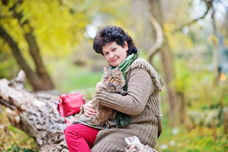 高级女人与秋天的公园里的猫