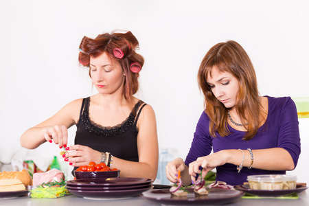 两个年轻漂亮的女人家庭主妇烹饪与头发上的卷发