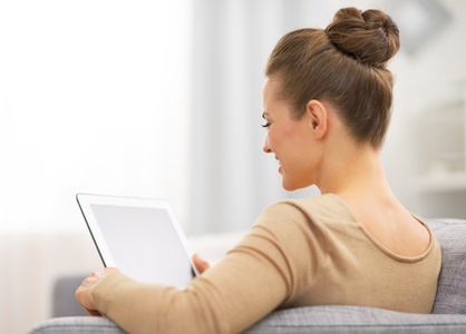 年轻的女人坐在沙发上，使用 tablet pc。后方的看法