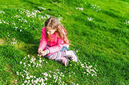 漂亮的小女孩在一个早期的春天，阳光明媚的日子玩花在公园里穿着明亮的粉色外套