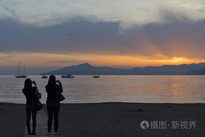 在日落时分在塞斯特海滩上接吻的男人和女人接球照片-正版商用图片1h