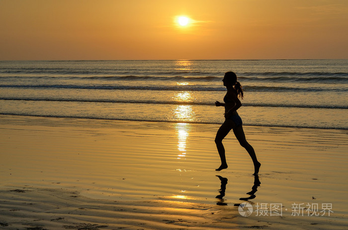 女人慢跑者在用反射的日落海滩上运行的剪影