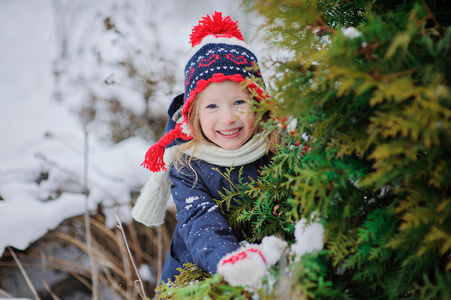 快乐的孩子女孩在红色和蓝色的针织帽，在白雪皑皑的冬季花园里散步