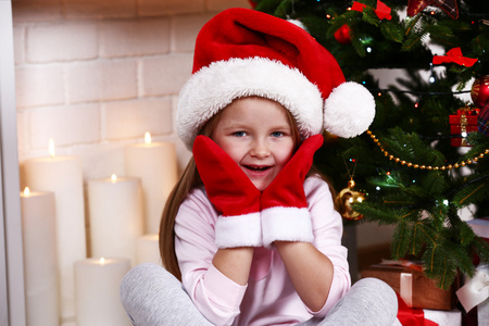 戴着圣诞帽和手套的小女孩坐在菲的杉树旁