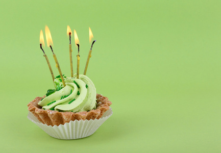 绿色背景上的蜡烛的生日杯蛋糕图片