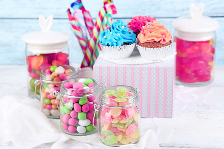 多色糖果的玻璃罐和纸杯蛋糕上颜色木制背景