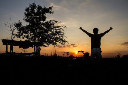 一个人的轮廓举起他的手，站在那里看看空中的太阳