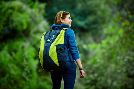 女人微笑着站在外面在森林里，背包里的徒步旅行者