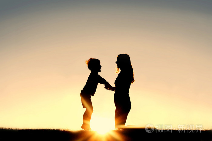 母亲和年幼的孩子,手牵着手在日落时的剪影