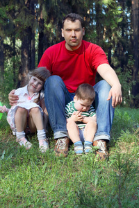 红色 t 恤与两个孩子的快乐年轻爸爸坐在草地上