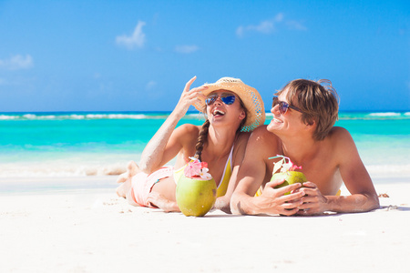 快乐的年轻夫妇躺在巴巴多斯的热带海滩上和喝椰子鸡尾酒