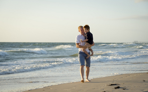 年轻快乐的父亲在他拿着武器小儿子在沙滩在海浪上行走