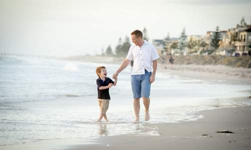 快乐的父亲牵握的小儿子在海滩上，赤脚走在一起