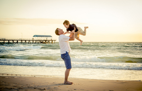 年轻快乐的父亲，在他举起武器小儿子把他放在沙滩上