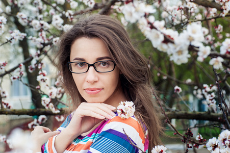 美丽的女人，戴眼镜的但在背景上的一棵开花的树