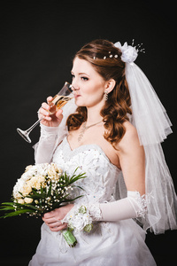 时装模特与黑色演播室背景在喝香槟，身穿婚纱的新娘花束