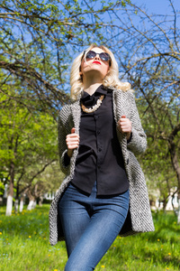 在外套 牛仔裤 太阳镜在晴朗的一天在公园散步美丽年轻快乐金发女郎