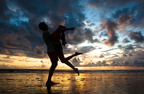 落日下的剪影的年轻夫妇在爱拥抱在海滩