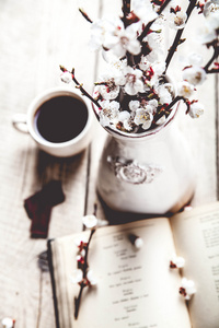 老式开卷与樱桃树开花分支上的木桌和一个美丽的古董花瓶。一杯咖啡