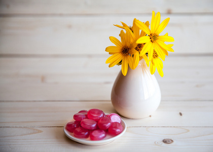 黄色的花，在一个古董花瓶，木制的背景上的红色糖果