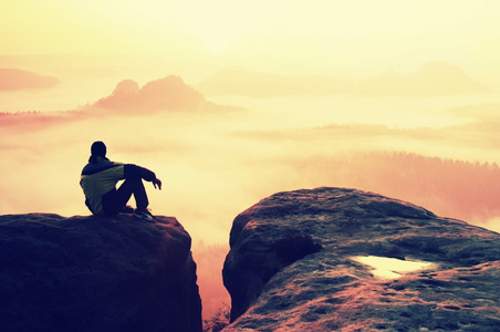 后方的看法的男性徒步旅行者在享受多彩黎明 mounrains 山谷上空同时坐在岩石峰值