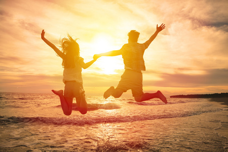 年轻幸福的夫妇在海滩上跳跃图片
