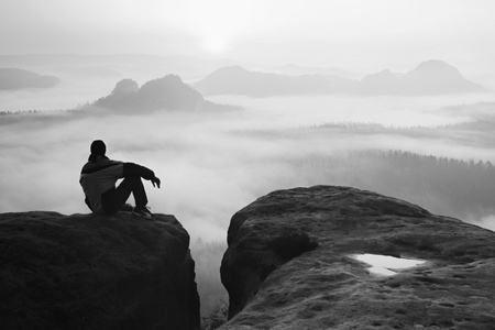 后方的看法的男性徒步旅行者在享受多彩黎明 mounrains 山谷上空同时坐在岩石峰值