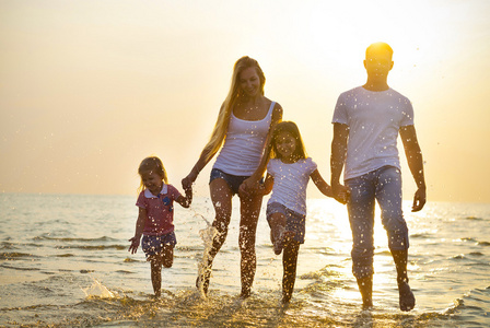 幸福开心的年轻家庭在日落时在海滩上运行。家庭