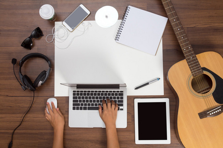 使用笔记本电脑的原声吉他和耳机的办公室桌子背景手