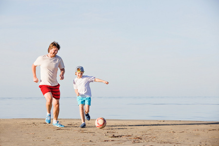 快乐的父亲和儿子踢足球或橄榄球在沙滩上