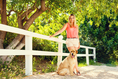 美丽的年轻女孩的肖像与她的狗拉布拉多猎犬户外在夏季美丽的公园