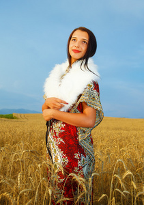 一位年轻女子，穿着装饰性的连衣裙，穿着白色的毛皮，站在W上