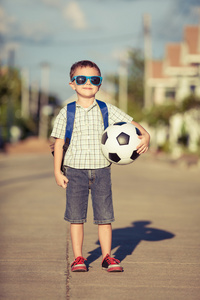白人小男孩站在路上，抱着他的足球