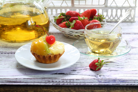 在透明的杯子里喝茶, 吃一个带水果的蛋糕和一个新鲜的草莓