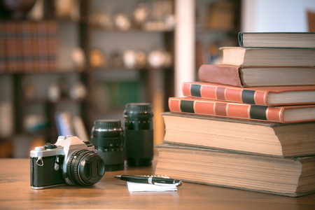 一叠旧书籍和旧相机在木桌前，复古的滤波图像