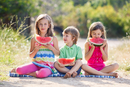 三个快乐微笑儿童吃西瓜在公园图片