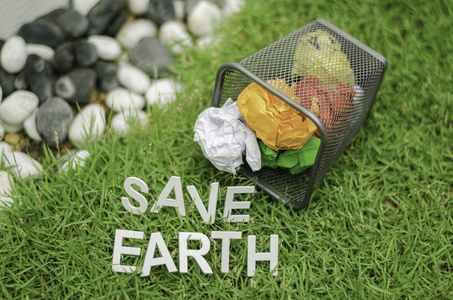 垃圾桶上的彩色球废纸的顶视图。在绿草上拯救地球的词
