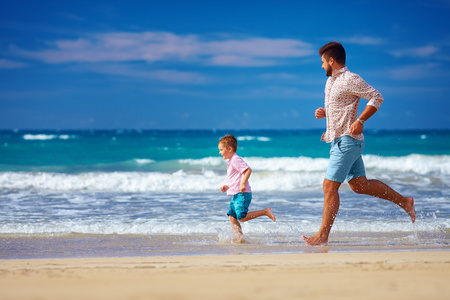 快乐兴奋的父亲和儿子运行在夏天的海滩，享受生活
