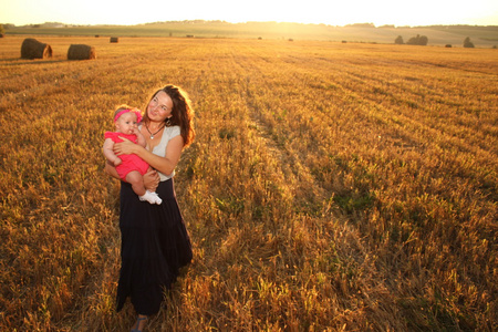 幸福的母亲抱着婴儿的微笑在阳光下的麦田。室外拍摄