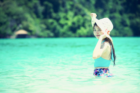 亚洲美丽的年轻女子头戴帽穿比基尼在海滩上