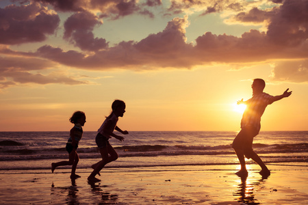 父亲和孩子们在日落的时候在海滩上玩