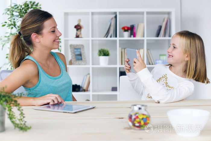 年轻的母亲和女儿玩数字平板电脑在家里照片-正版商用