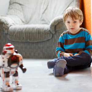 小金发男孩玩耍着机器人玩具在家，室内