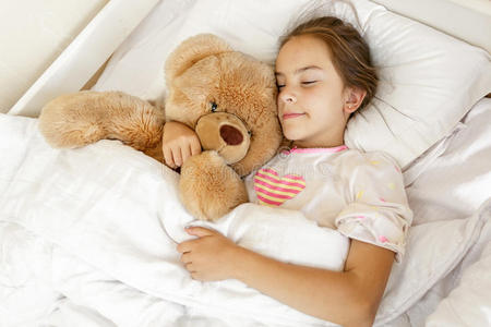 可爱的女孩睡在床上拥抱着大泰迪熊