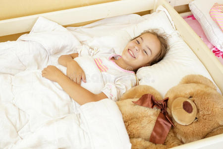 微笑的女孩和大泰迪熊躺在床上