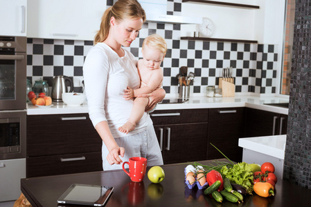 母亲抱着女儿在厨房做一顿饭的新鲜蔬菜和水果。母亲和女儿在厨房里拿着一个苹果。健康食品和健康的生活理念