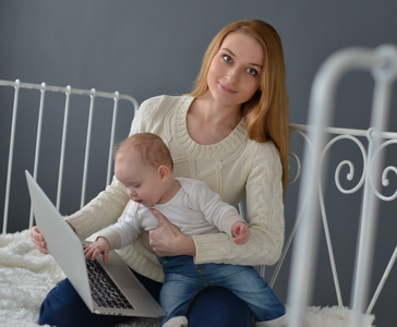 婴儿和笔记本电脑坐在家里的床上的女人