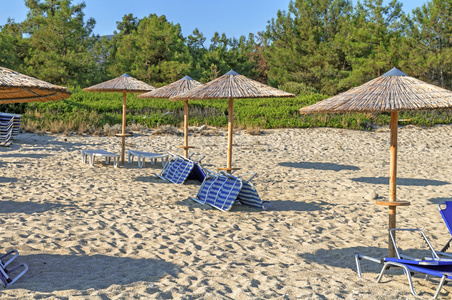 日光浴浴床，在希腊的美丽海滩背景上的稻草伞