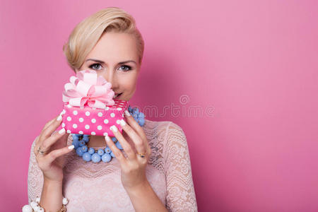 生日快乐。可爱的金发女人拿着一个带缎带的小礼盒。柔和的颜色