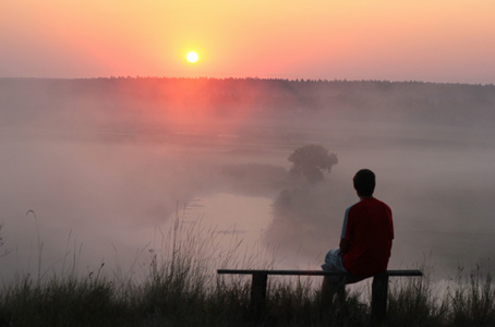 男人坐在长椅上，看着朦胧的日出